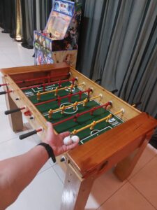 Foto de uma mesa de totó de madeira, com jogadores de plástico azuis e vermelhos, um clássico indispensável no aluguel de brinquedos para eventos.