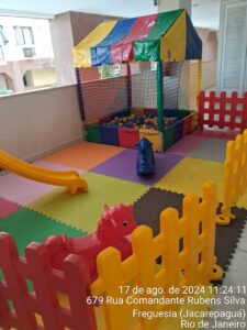 Foto de um kit área baby montado para locação, incluindo um escorregador colorido, piscina de bolinhas, gangorra, tapetes de EVA e cercado de grades."